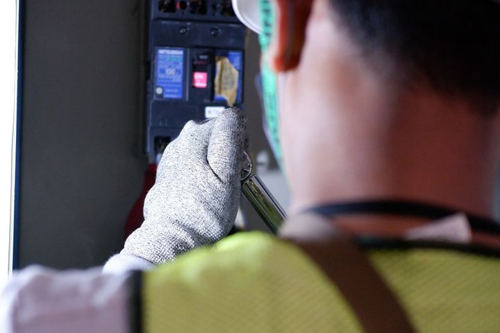 Electrician checking a circuit breaker box Electrician wearing gloves working on a home circuit breaker box