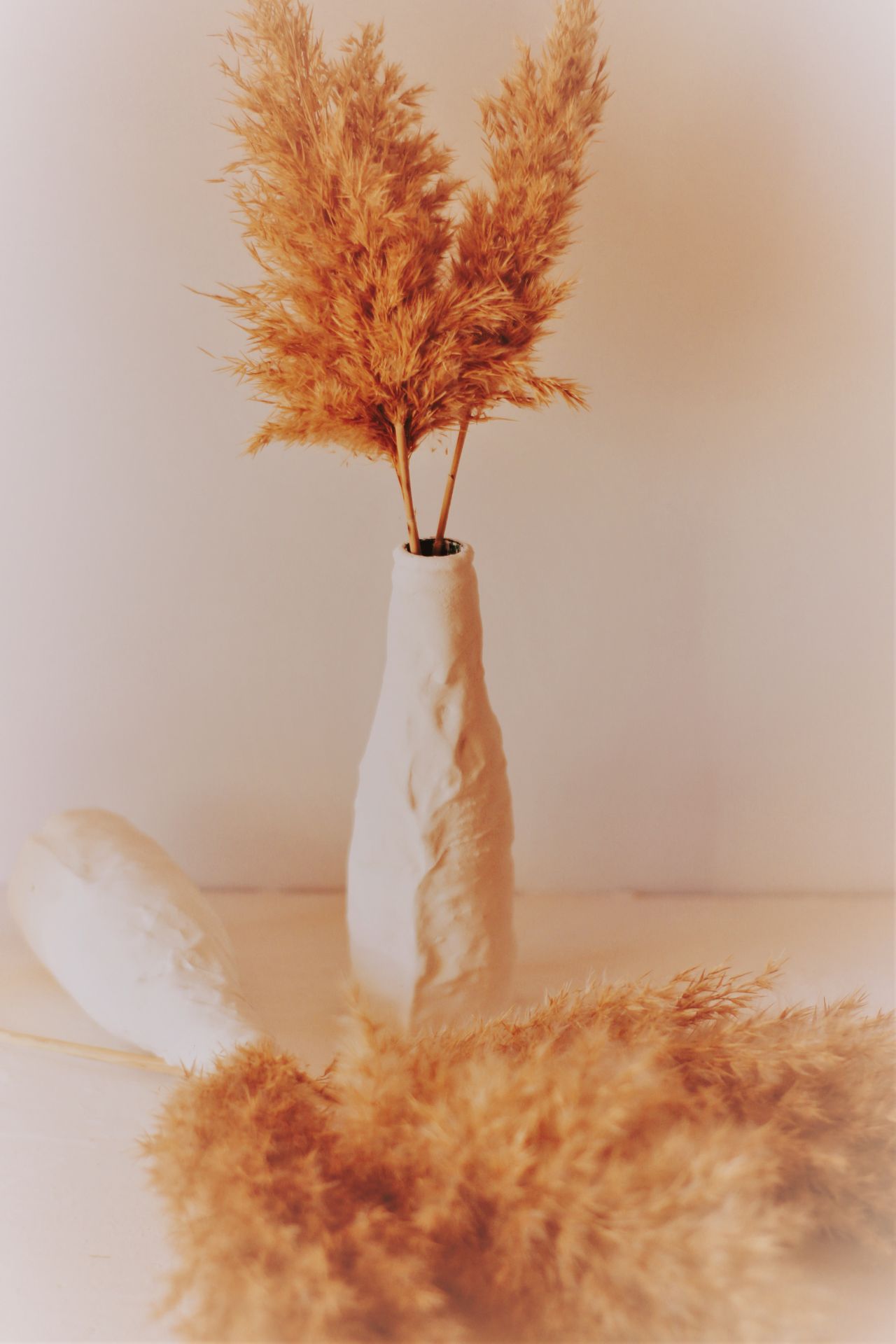 Tall dried pampas grass plumes in a white vase with loose stems in the foreground