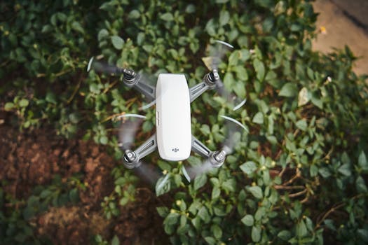 High-angle shot of a white drone flying over lush green foliage outdoors.