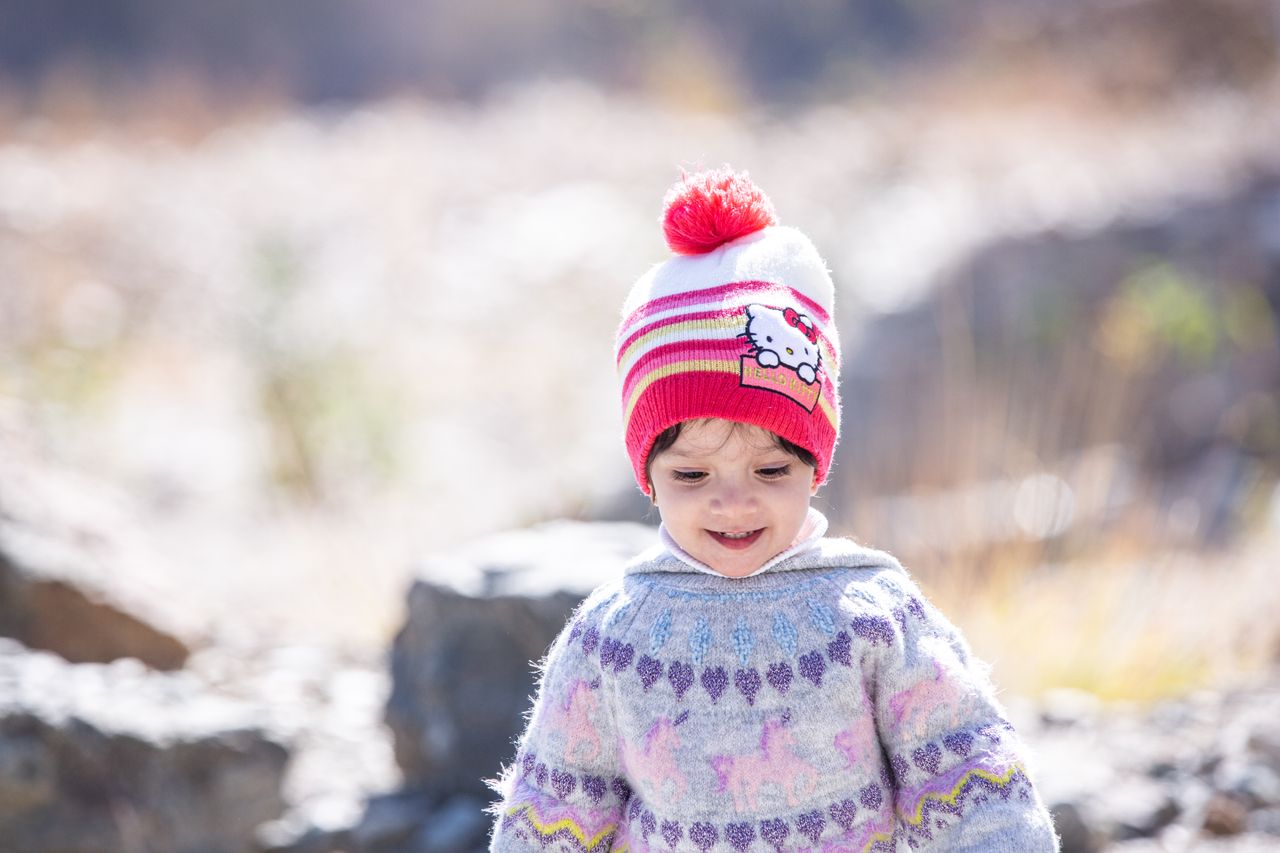 Toddler in a patterned knit sweater and striped pom-pom hat on a bright winter day