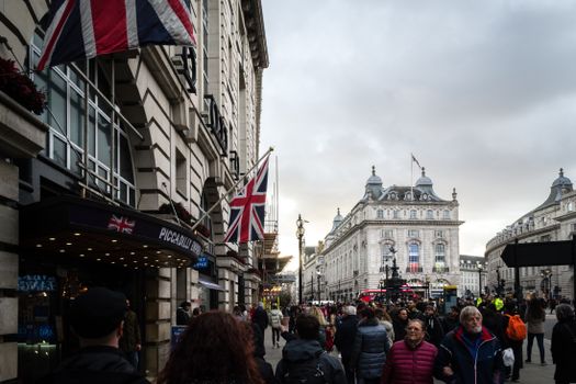 A bustling street scene at Piccadilly Circus, London, with iconic architecture and Union Jack flags.
