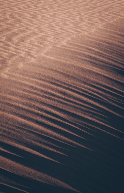 Captivating twilight view of textured sand dunes casting long shadows, creating a serene desert landscape.