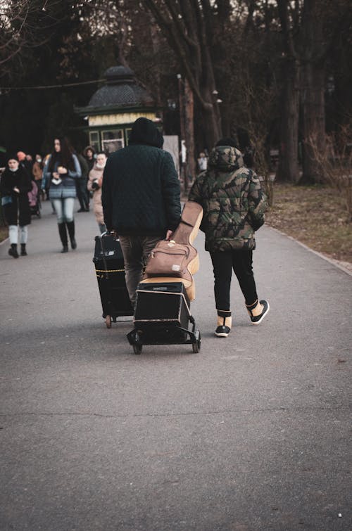 Two People in Hoodie Jackets Walking on Road Carrying Luggage