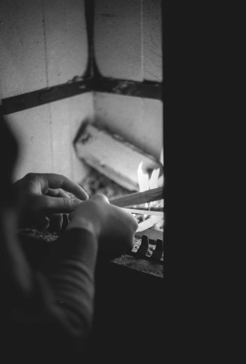 Grayscale Photo of a Person Holding a Wood in Fireplace