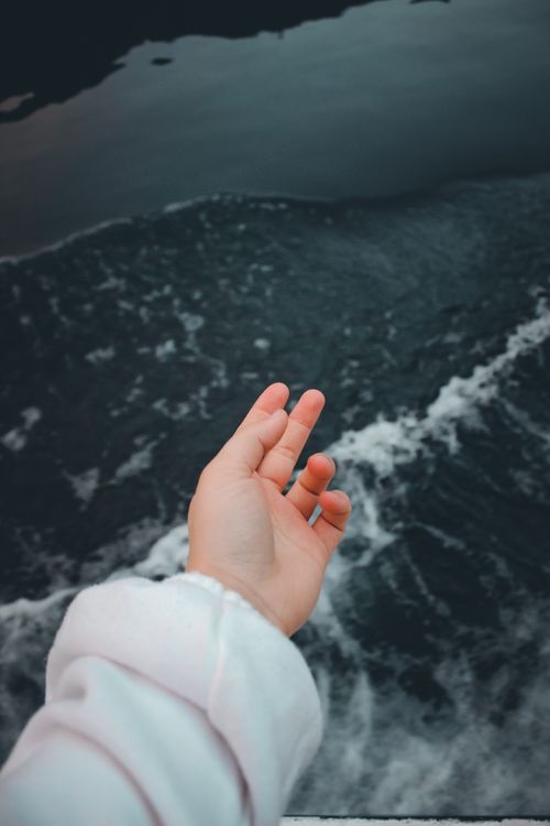 Free A hand in a white sleeve reaching over moving ocean waves, evoking a sense of freedom. Stock Photo