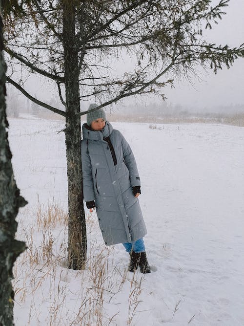 A Woman in Gray Coat Standing on Snow Covered Ground