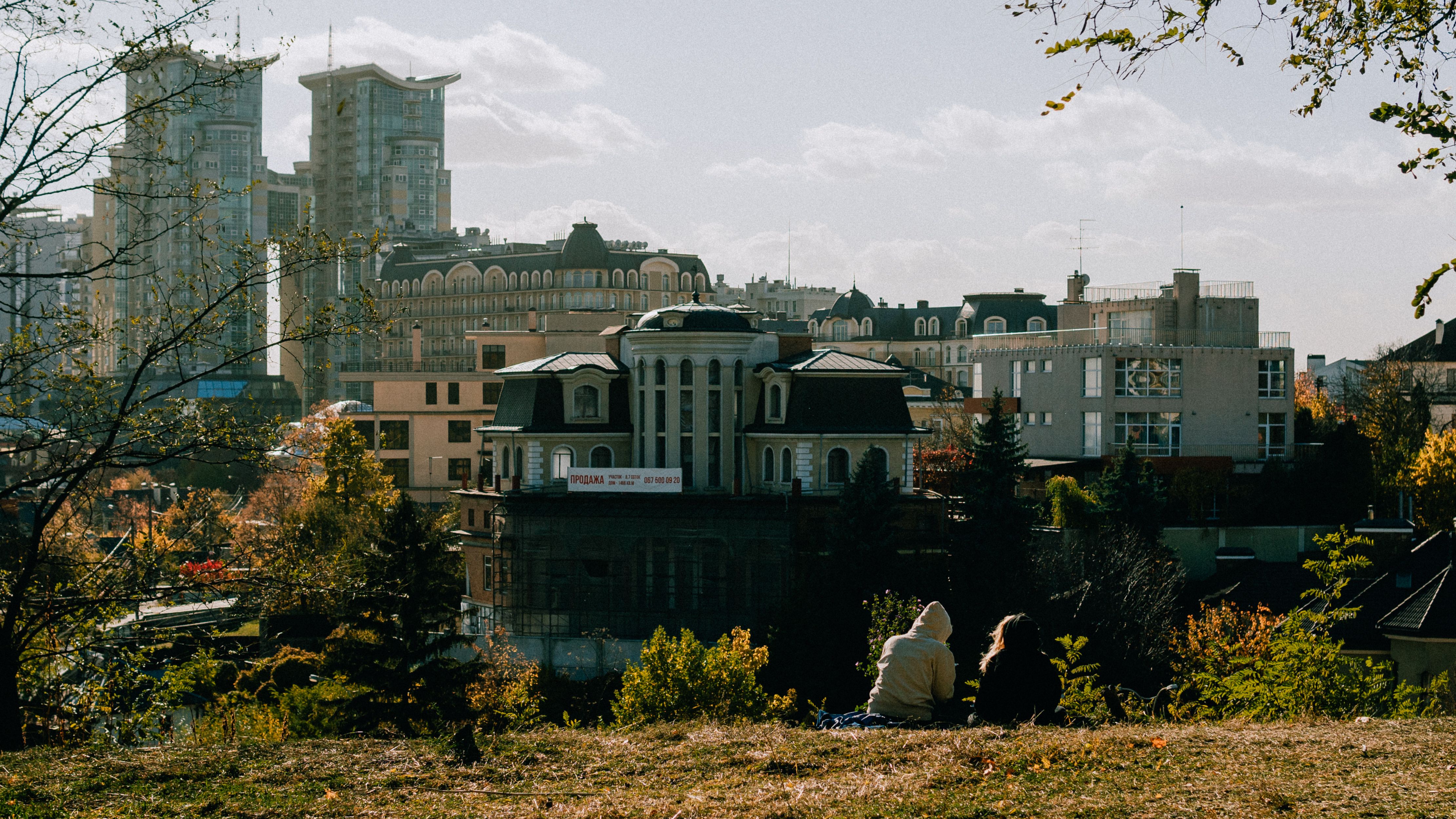 A couple enjoys a relaxing moment outdoors while overlooking the Kyiv cityscape on a sunny day.