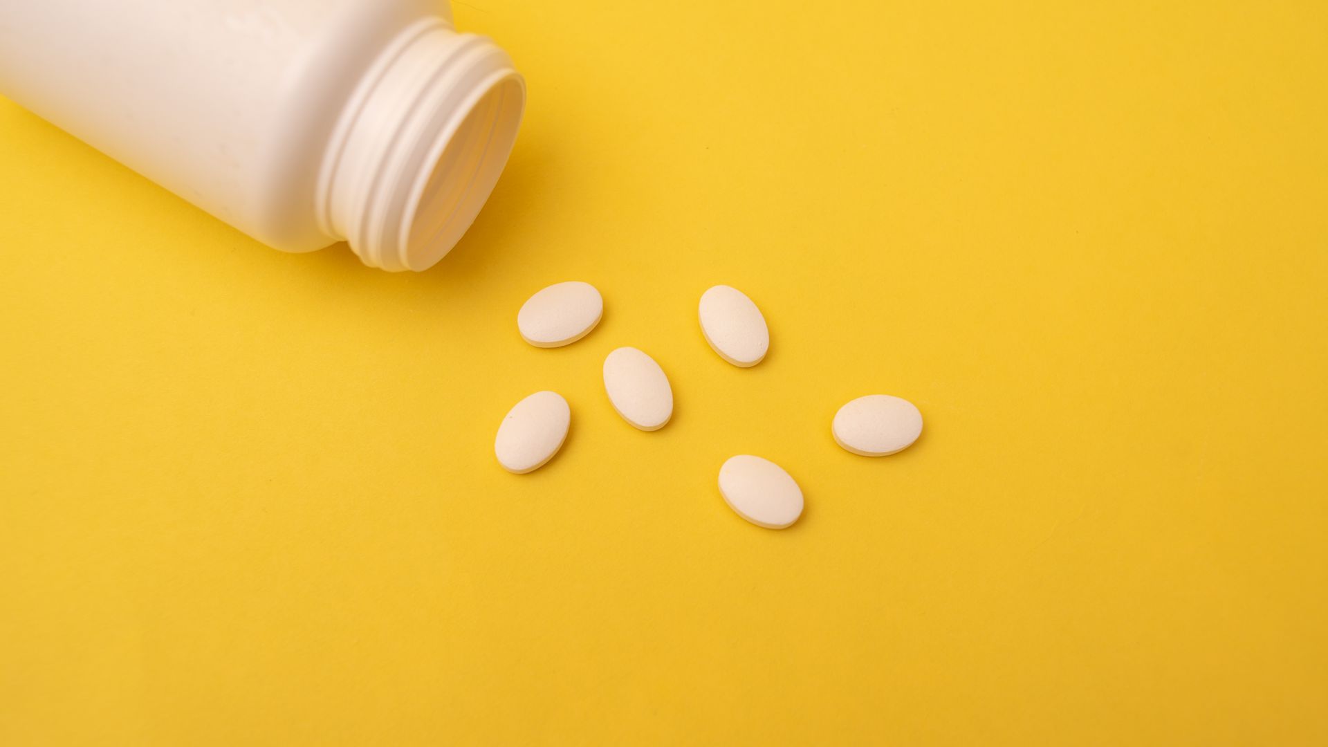 Sun Pharma Modafinil: A Comprehensive Guide White pills spilling from a plastic bottle on a vibrant yellow background, conveying health and medication themes.
