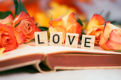 Free Close-up of wooden blocks spelling LOVE surrounded by vibrant orange roses. Stock Photo