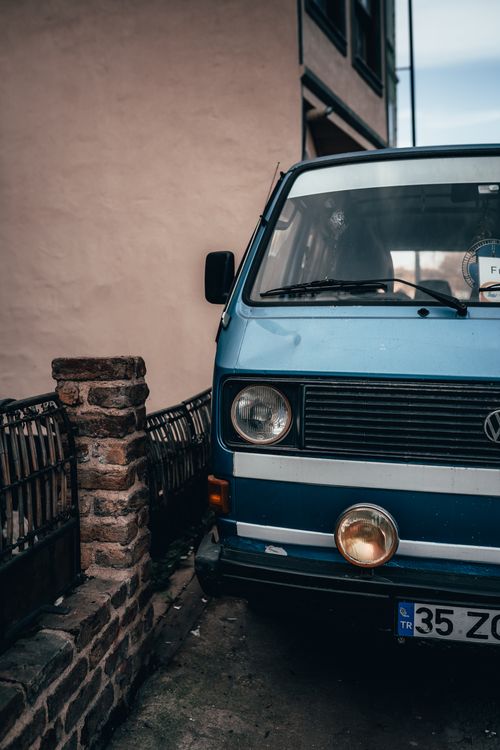 Free Close-up of a vintage blue van parked beside an urban brick wall on a cloudy day. Stock Photo