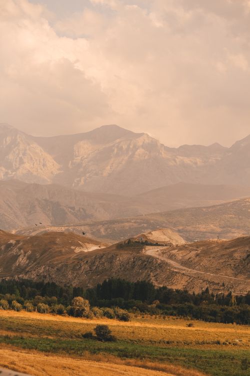 Free A tranquil mountainous landscape with rolling hills under a cloudy sky, captured at dusk. Stock Photo