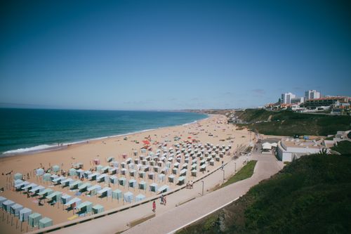 Free Aerial view of a sunny beach resort with people, umbrellas, and ocean waves. Stock Photo