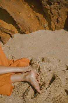 Serene close-up of crossed legs and bare feet on sandy beach, perfect for relaxation themes.