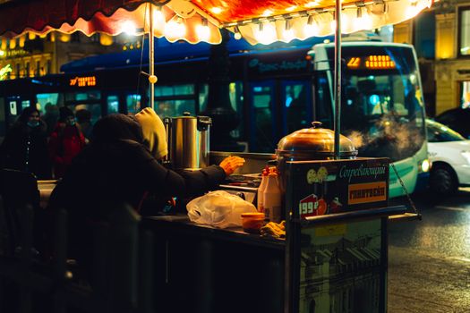 A bustling night scene in Saint Petersburg, featuring a street vendor with steam rising from hot food.