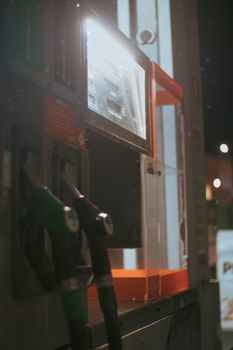 Close-up of a gas station fuel pump illuminated at night, showcasing nozzles and signage.