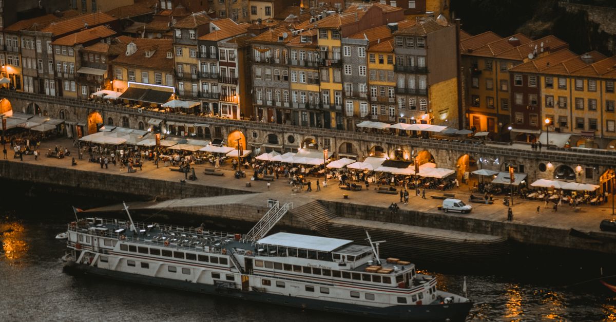 Aerial view of Porto riverside at night with moored cruise ship and vibrant promenade.