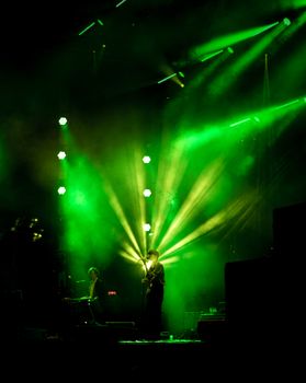 Energetic stage performance with striking green lighting and dynamic musician presence.