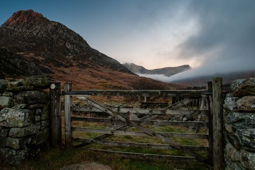 Free A serene scene featuring a rustic wooden gate and mountains under an overcast sky. Stock Photo