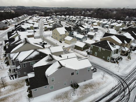 Drone view of suburban houses covered in snow during winter, showcasing a quiet residential neighborhood.