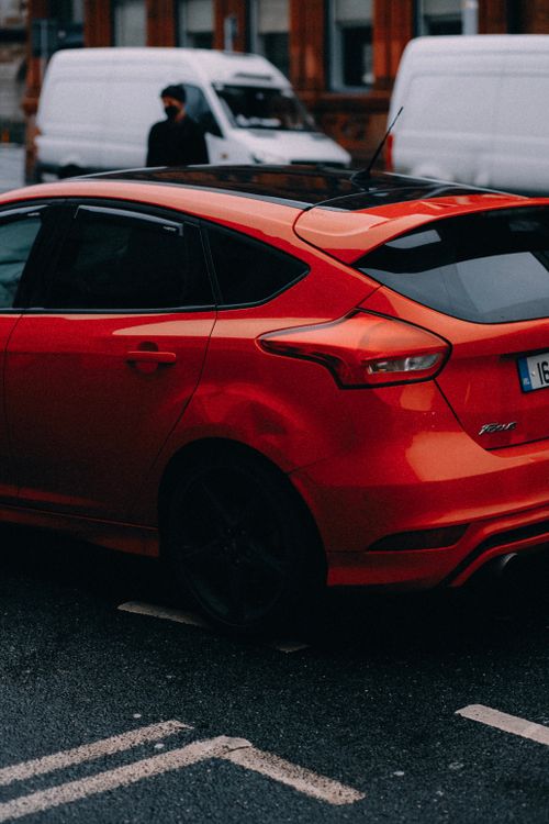Free A vibrant red Ford Focus parked on a wet city street, capturing urban life. Stock Photo