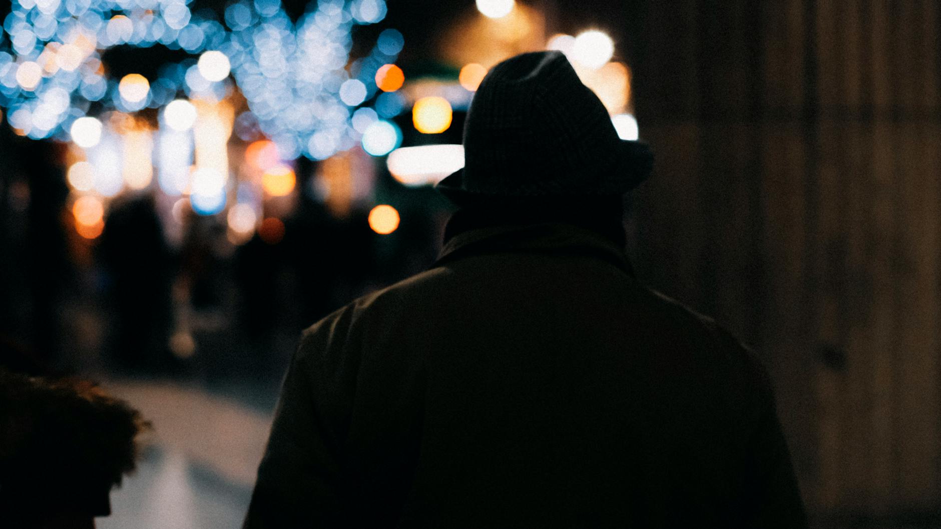 Karanlık ve puslu bir atmosferde, uzaklardaki zayıf bir ışık hüzmesine doğru sessizce ve umutla bakan yalnız bir insan silüeti.