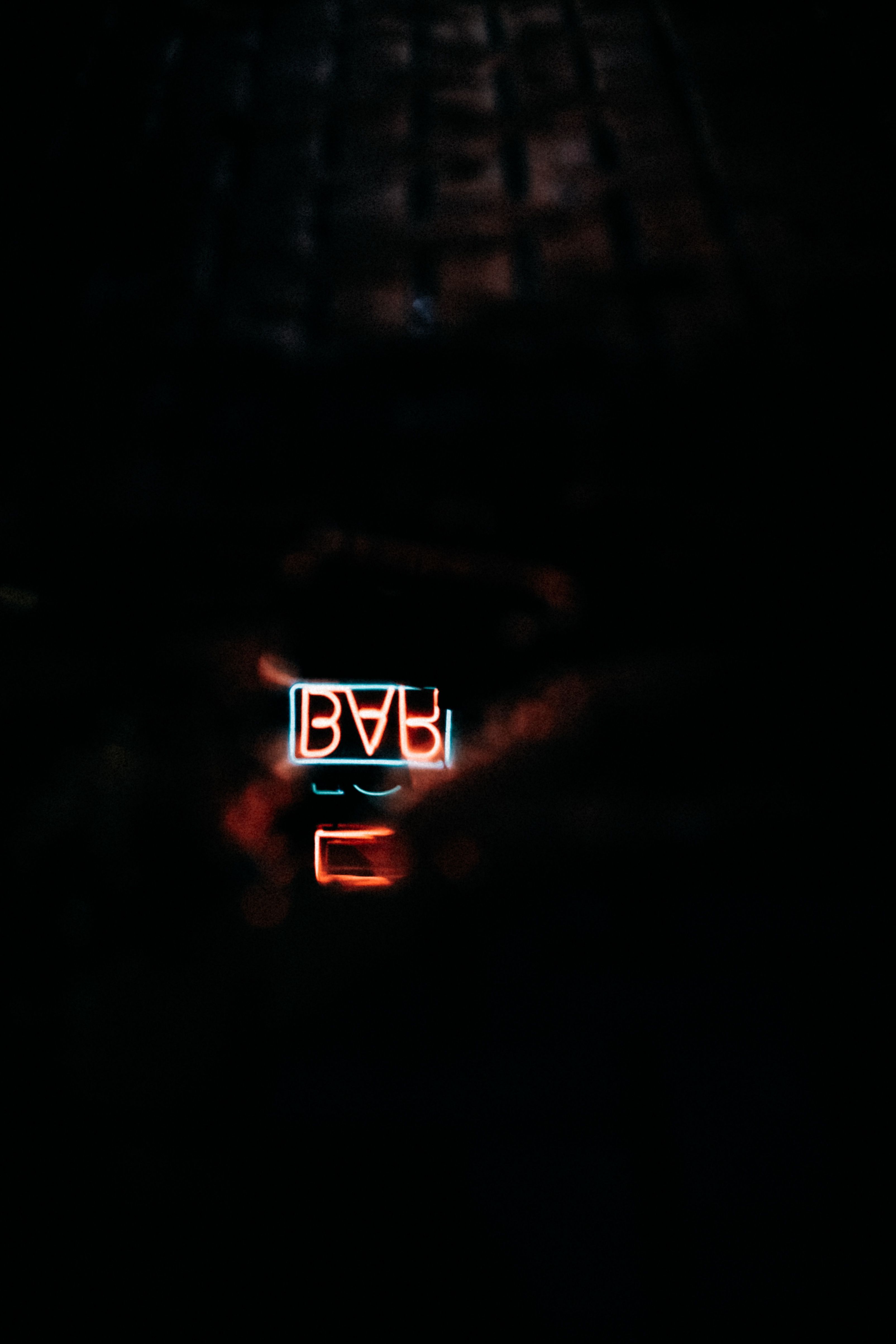 A neon bar sign reflected in a puddle at night, emitting a moody glow.