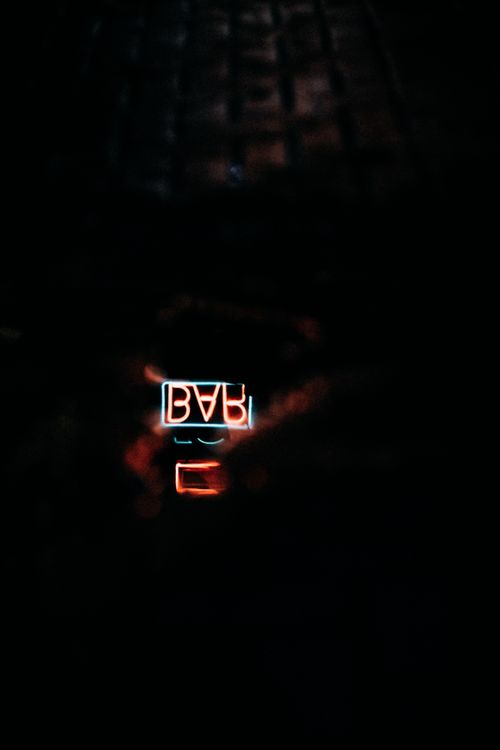 Free A neon bar sign reflected in a puddle at night, emitting a moody glow. Stock Photo