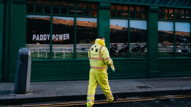 City worker in yellow uniform passing by a Paddy Power storefront window, reflecting urban life.
