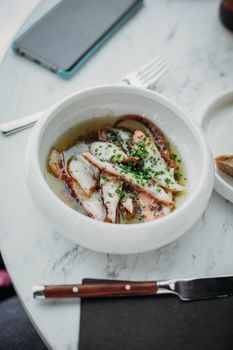 A mouthwatering seafood soup served in a white bowl on a marble table, paired with a smartphone.