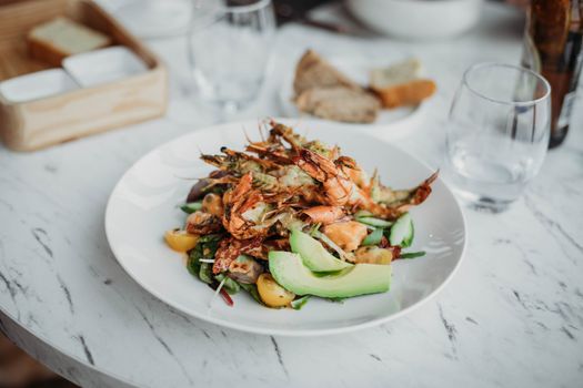 A vibrant seafood salad with shrimp, avocado, and tomatoes served on a white plate.