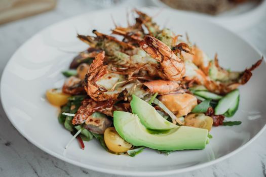 Delicious fresh seafood salad with grilled shrimp and avocado on a white plate.