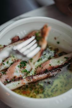 Close-up of grilled squid in a bowl with herb oil, garnished with chives.