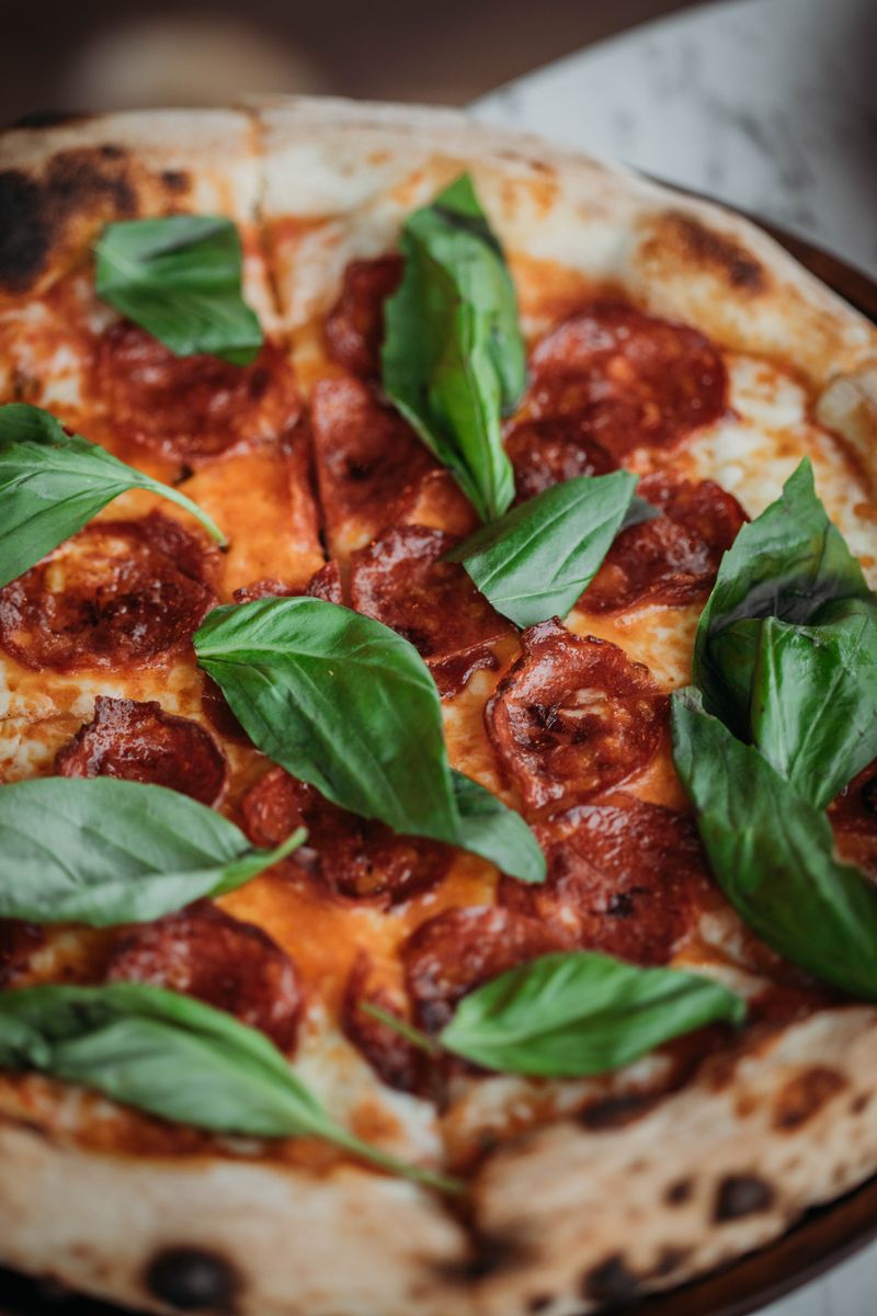 Pizza s pepperoni salámem a čerstvými lístky bazalky v detailu