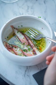 Close-up of grilled squid served in garlic and herb olive oil in a white bowl.