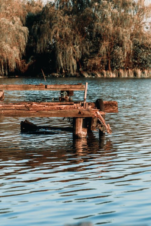 Free Peaceful scene with a weathered wooden jetty over a calm lake at sunset. Stock Photo