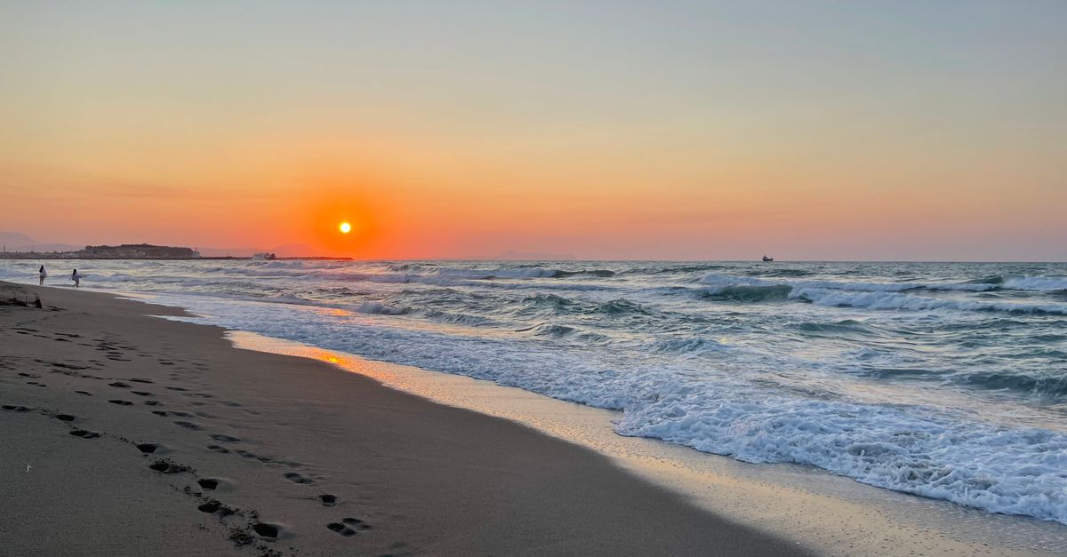A tranquil beach sunset in Rethimno, Greece with footprints in the sand and gentle ocean waves.