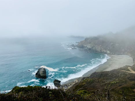 A scenic view of San Francisco's foggy coastline, emphasizing rocky cliffs and blue ocean waves.