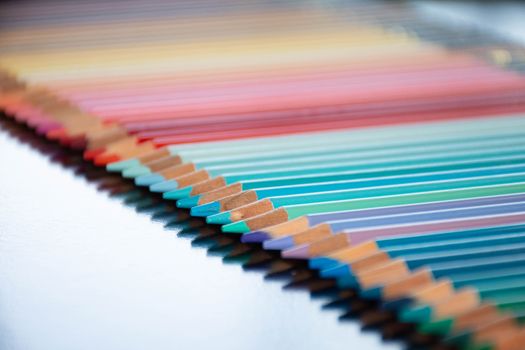 Vibrant row of sharpened colored pencils showing a spectrum of hues, perfectly aligned on a reflective surface.