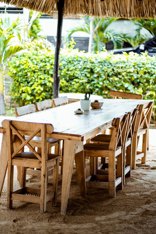 Free Wooden table and chairs under a thatched roof in a lush outdoor setting. Stock Photo