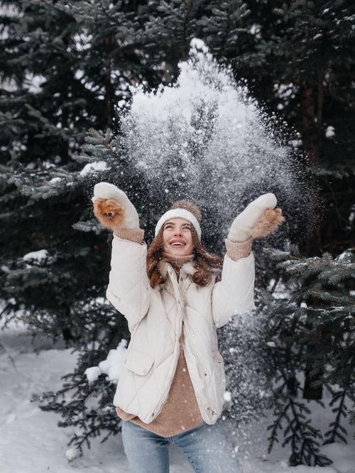 Free A woman in winter attire joyfully playing with snow amidst a snowy forest, expressing excitement. Stock Photo