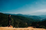一个人站在山顶上，俯瞰着晴朗天空下广阔的山区秀丽风景