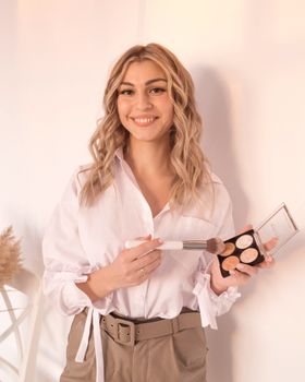 Smiling woman demonstrating makeup application with a brush set indoors.