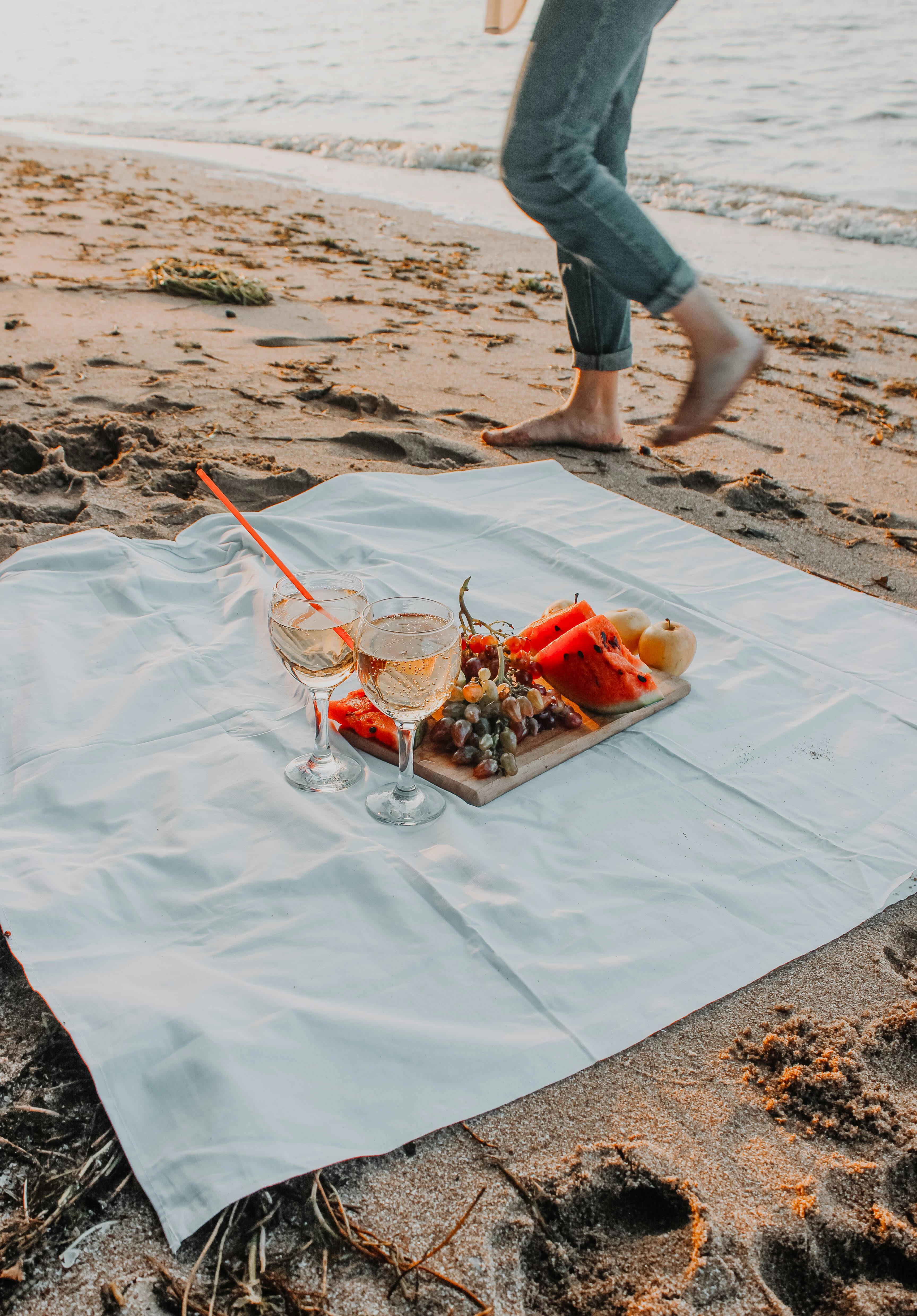 Enjoy a relaxing beach picnic with wine and fresh fruits on a serene shoreline.