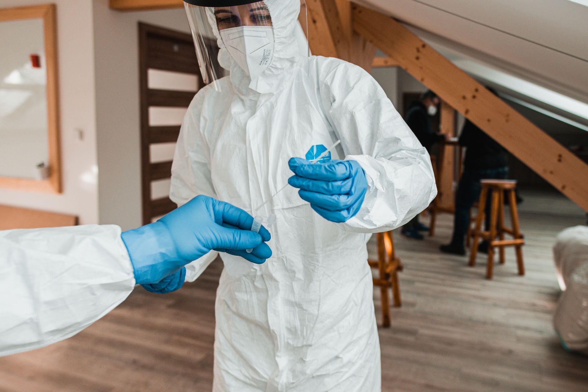 Healthcare worker in protective gear conducting a COVID-19 test indoors. Safety measures in place.