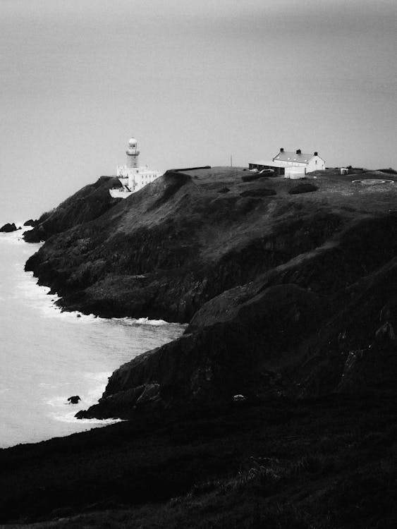 Black and White Photo of the Mountains by the Sea with Light House