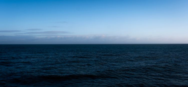 A tranquil ocean view under a twilight sky with calm waters and subtle waves.