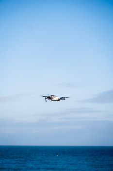 An aerial shot of a drone soaring over the ocean under a clear blue sky.
