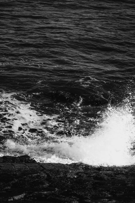 Monochrome image capturing waves crashing against a rocky shore with dramatic splash.
