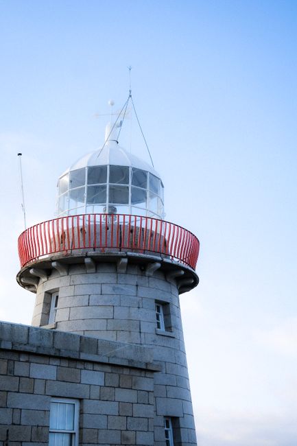 Close-up of a sturdy lighthouse tower with a red railing under a clear blue sky.
