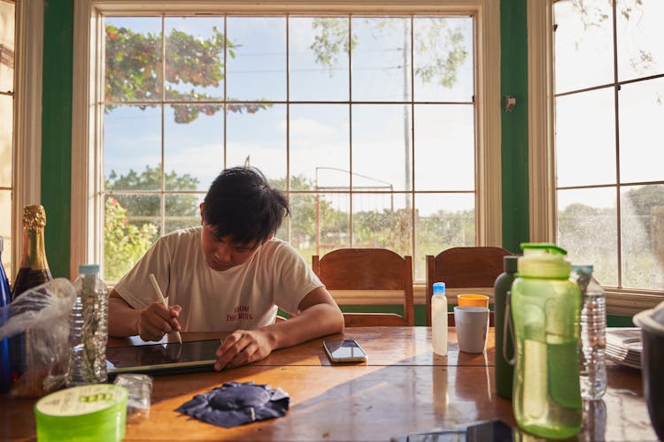 Young Man Sitting At A Table And Drawing On A Tablet 